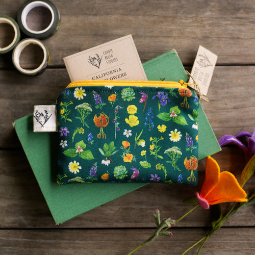 Load image 1 in gallery view. Dark green pouch with native wildflowers and a golden yellow zipper on a wooden background. 