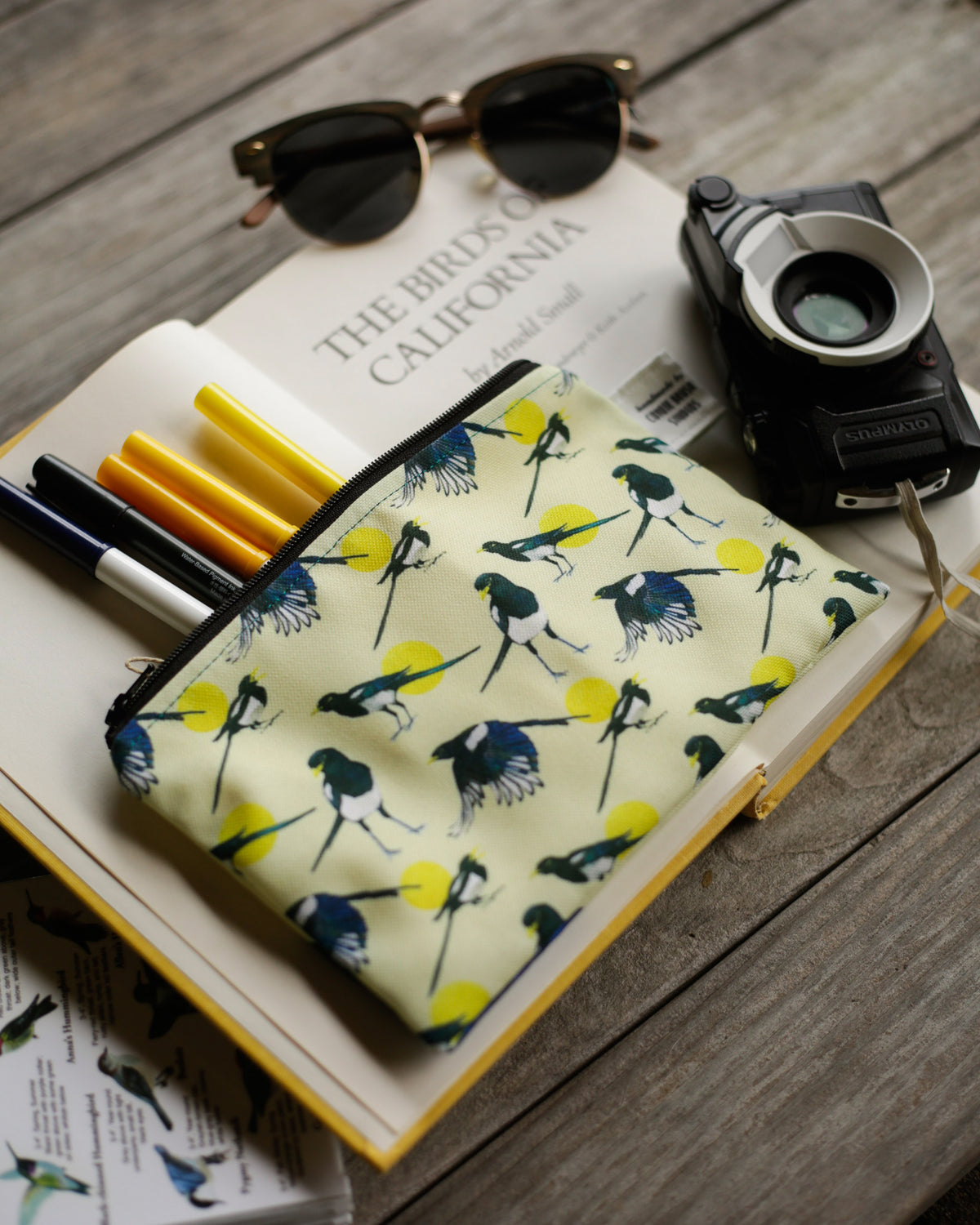 Back of pouch with a pattern of standing magpies and magpies in flight next to a camera.